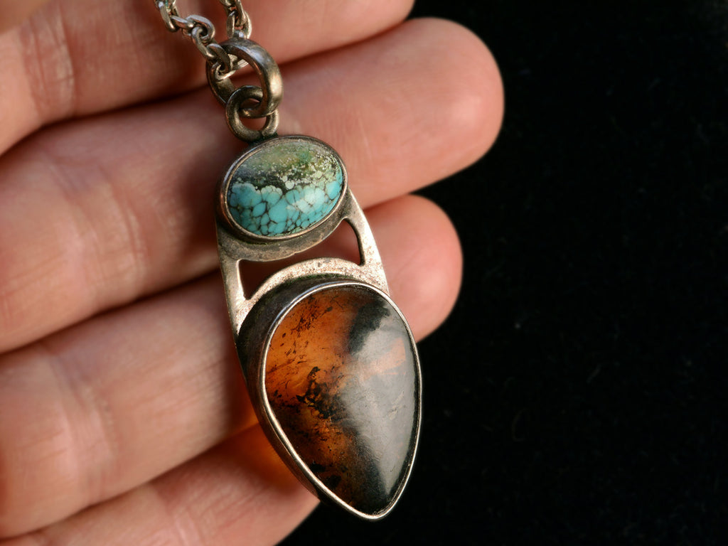 Silver pendant with oval turquoise and pear shaped tortoiseshell, held in hand.