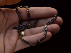 thumbnail of An antique chain of alternating silver and black striped links and gold filled links. Shown held in hand.