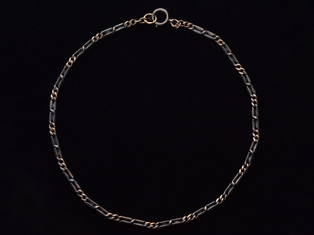 An antique chain of alternating silver and black striped links and gold filled links. Shown laid out on black background.