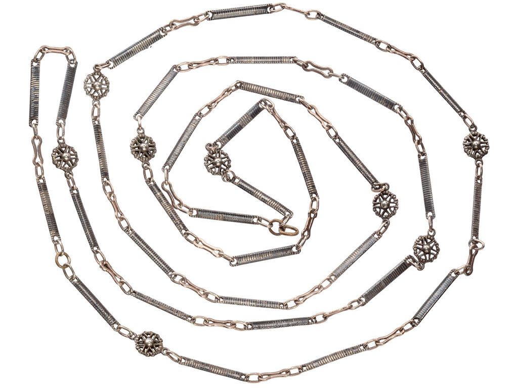 A 19th century long chain with alternating niello striped bar links, gold filled links, and silver rosettes, shown spiraled on white background.