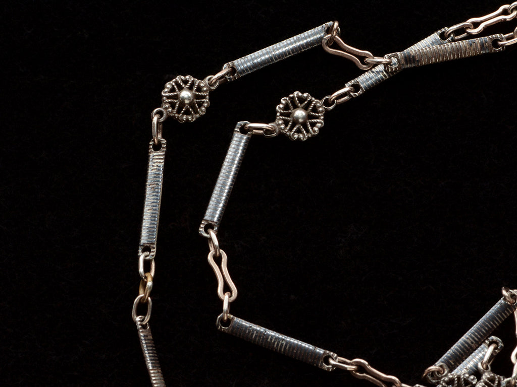 Detail of a 19th century long chain with alternating niello striped bar links, gold filled links, and silver rosettes, shown on black background.