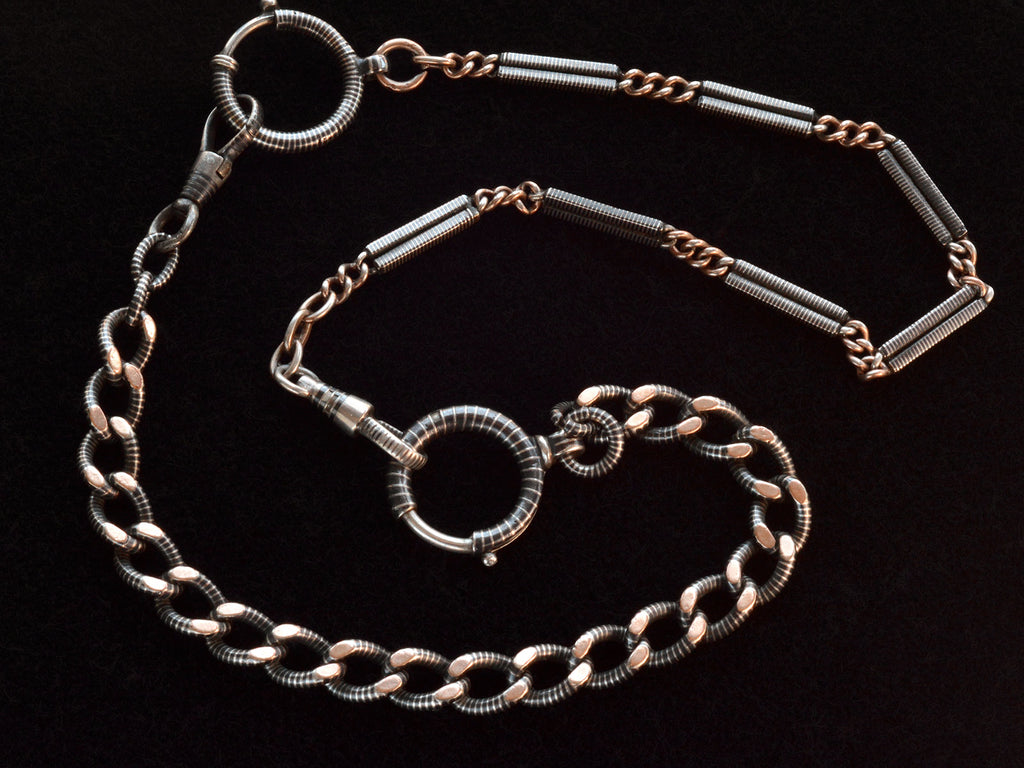 Close up of a necklace composed of a pair of gold filled and niello silver watch chains, on black background. 
