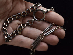 thumbnail of Close up of a necklace composed of a pair of gold filled and niello silver watch chains, shown held in hand.