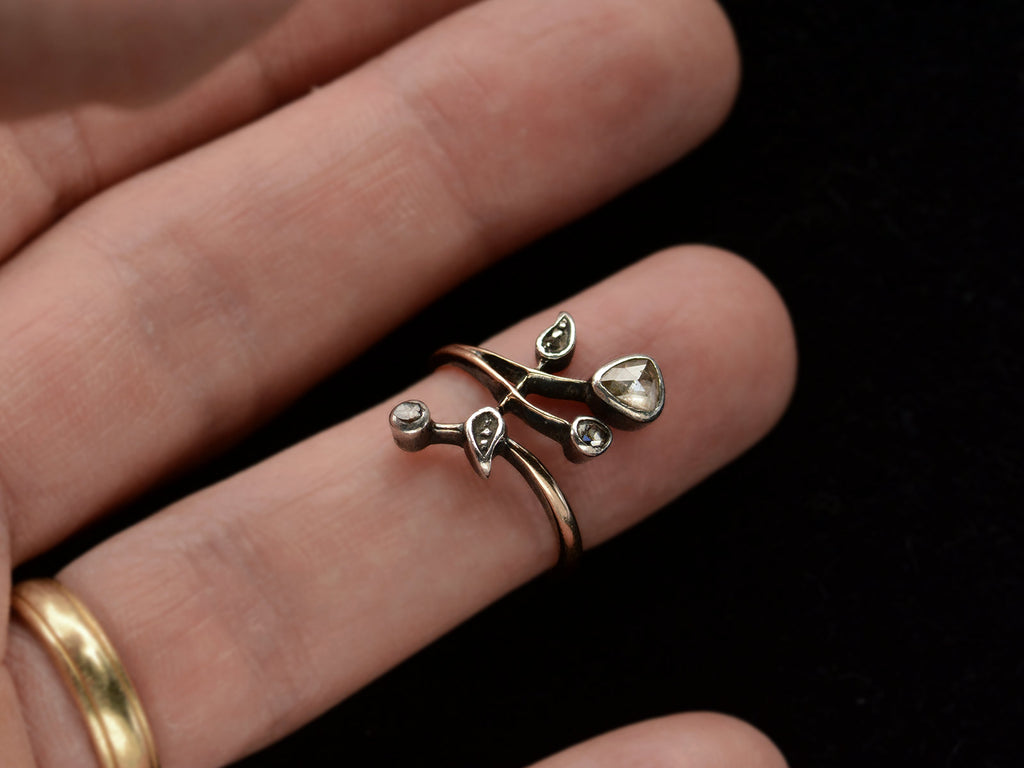 An antique Art Nouveau gold and silver ring with rose cut diamonds in a floral design. Shown on finger.