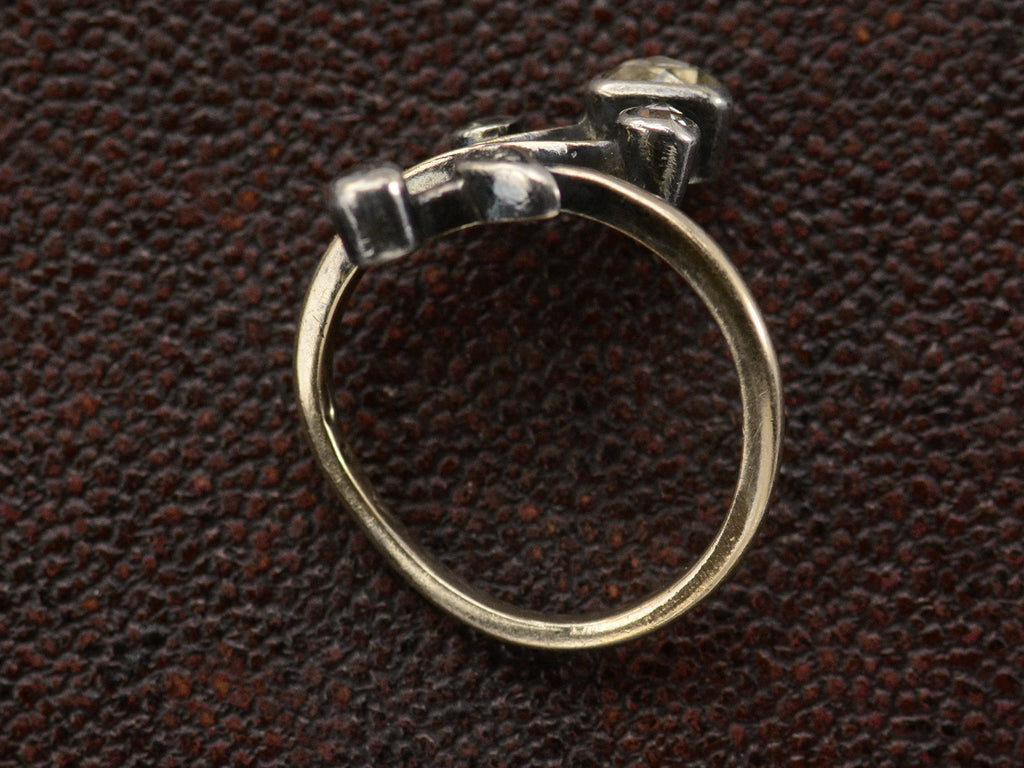 Side profile view of an antique Art Nouveau gold and silver ring with rose cut diamonds in a floral design. Shown on dark textured background.