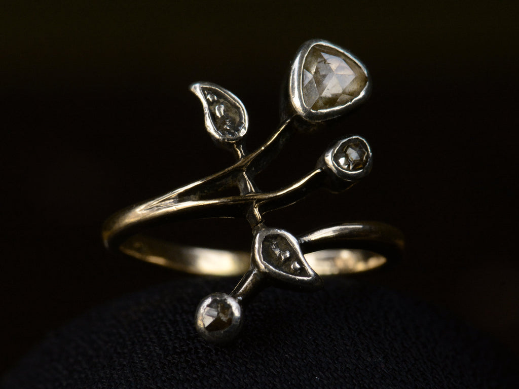 An antique Art Nouveau gold and silver ring with rose cut diamonds in a floral design. Shown on dark background.