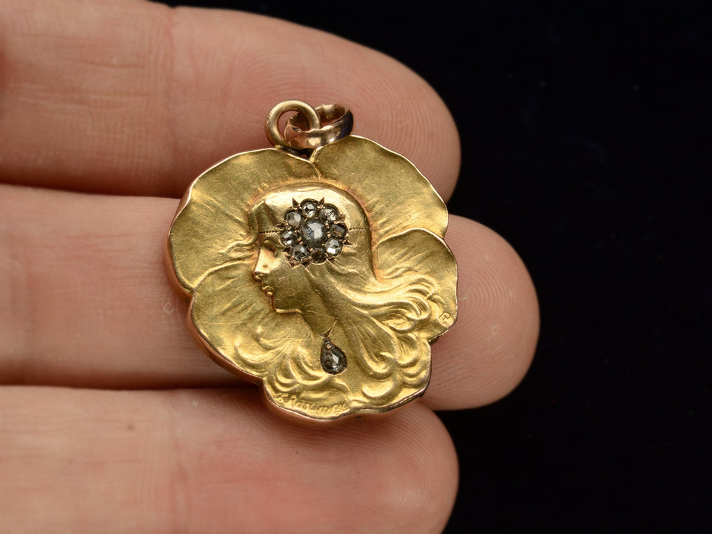 c1910 Art Nouveau yellow gold pansy shaped pendant with the profile of a woman (shown hand for scale)