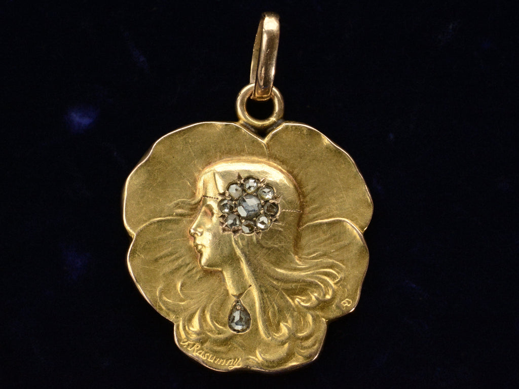 c1910 Art Nouveau yellow gold pansy shaped pendant with the profile of a woman (shown on black background)