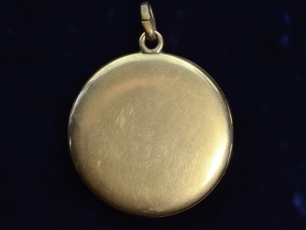 Backside of round vintage gilt brass locket. On dark background.