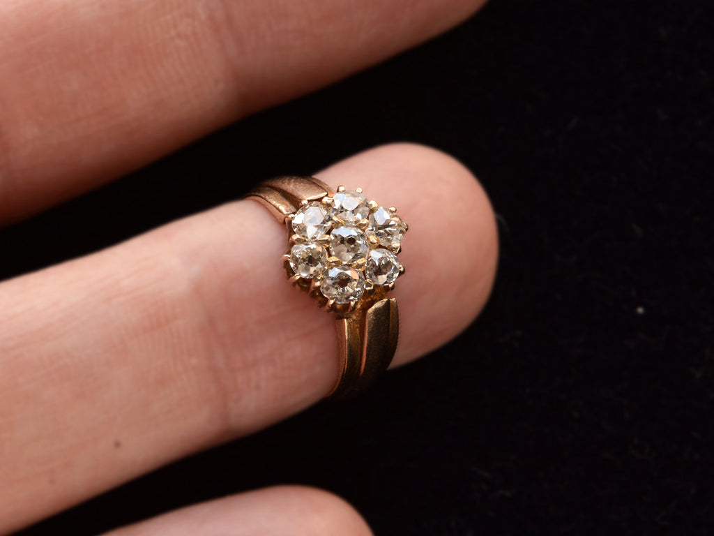 Front view of antique rosy-yellow gold ring with cluster of old mine cut diamonds, on finger