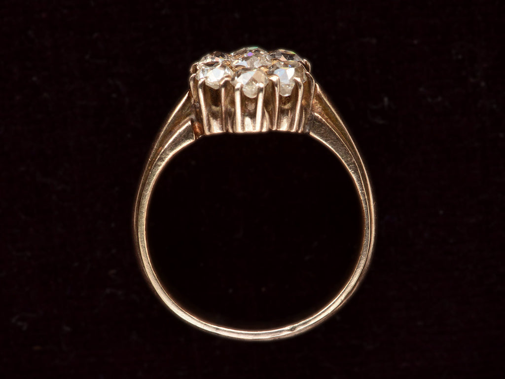 Side profile view of antique rosy-yellow gold ring with cluster of old mine cut diamonds, on black background.