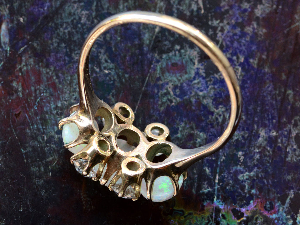 Inside view of a vintage gold ring featuring three oval white opal stones and four round diamonds, set in gold against a dark iridescent background.