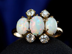 thumbnail of A gold ring featuring three oval white opal stones and four round diamonds, displayed on a black surface against a dark blue background.