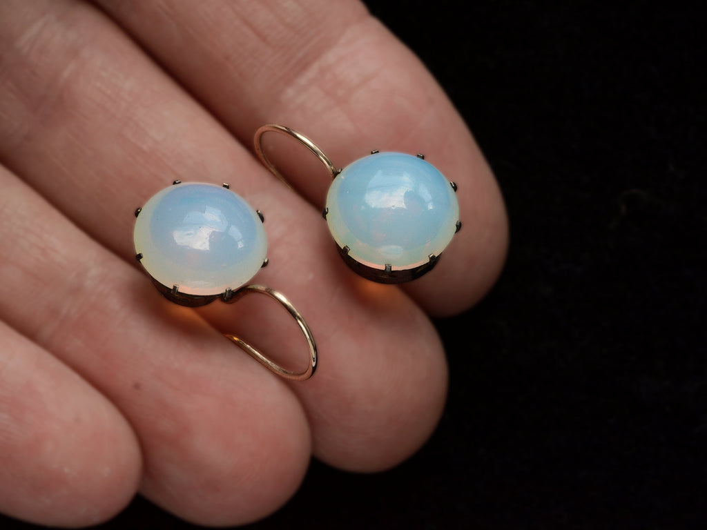 A vintage pair of round opaline glass earrings with blackened silver settings and 14K yellow gold ear wires. Shown on hand.
