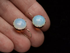 thumbnail of A vintage pair of round opaline glass earrings with blackened silver settings and 14K yellow gold ear wires. Shown on hand.