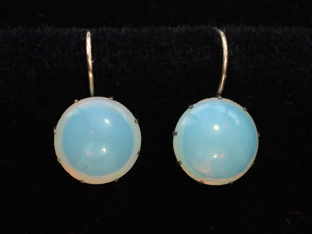 A vintage pair of round opaline glass earrings with blackened silver settings and 14K yellow gold ear wires. Shown on black background.