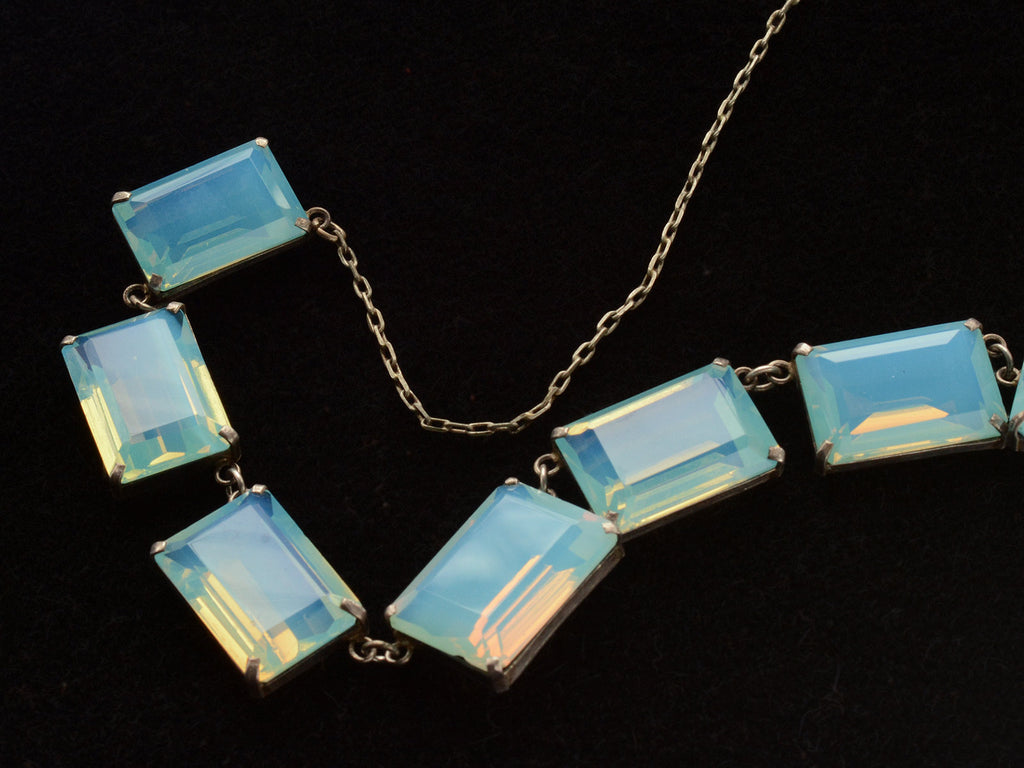 Detail view of vintage c1950 silver necklace with a bib of rectangular opalescent glass stones, shown on black background.