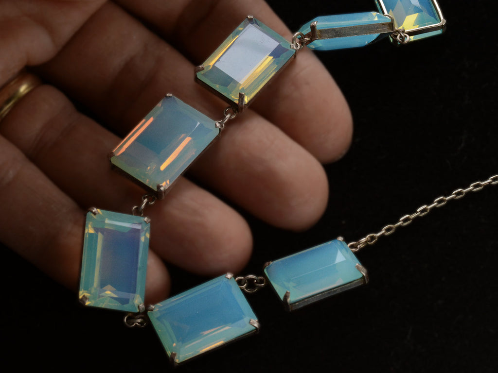 Detail view of vintage c1950 silver necklace with a bib of rectangular opalescent glass stones, shown in hand.