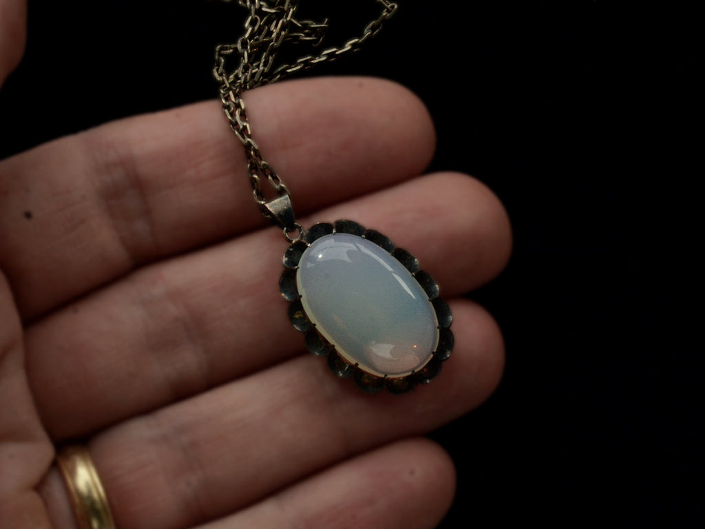 Detail of a vintage oxidized silver necklace with an oval opaline glass pendant, shown held in hand.