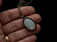 thumbnail of Detail of a vintage oxidized silver necklace with an oval opaline glass pendant, shown held in hand.