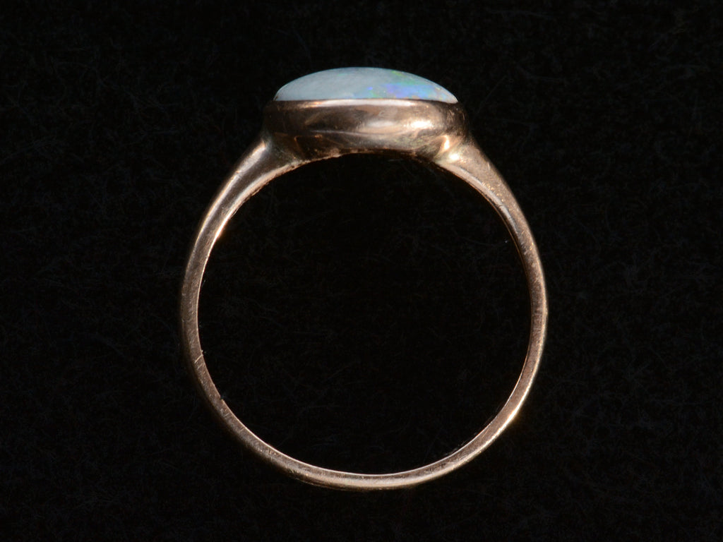 Side profile view of c1920 oval opal ring in rosy 10K gold, shown on black background.