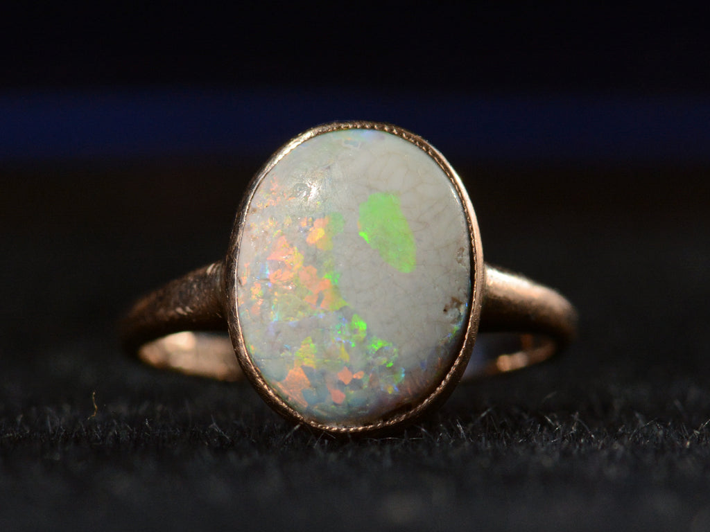 Front view of c1920 oval opal ring in rosy 10K gold, shown on black background.