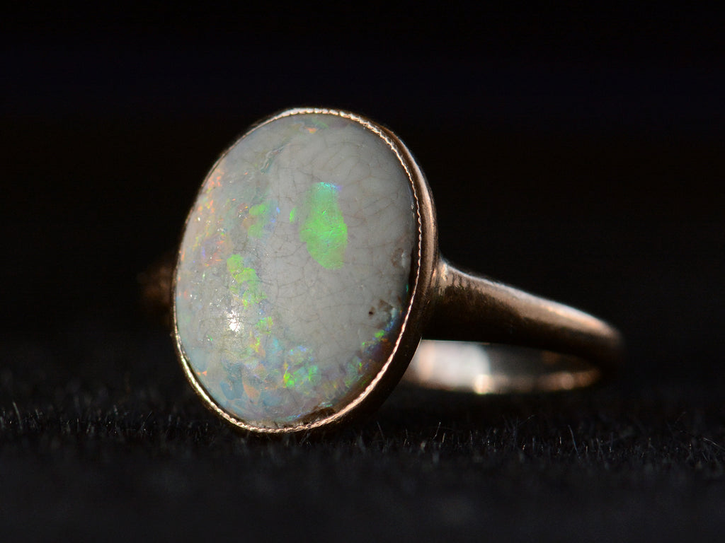 Right angled view of c1920 oval opal ring in rosy 10K gold, shown on black background.