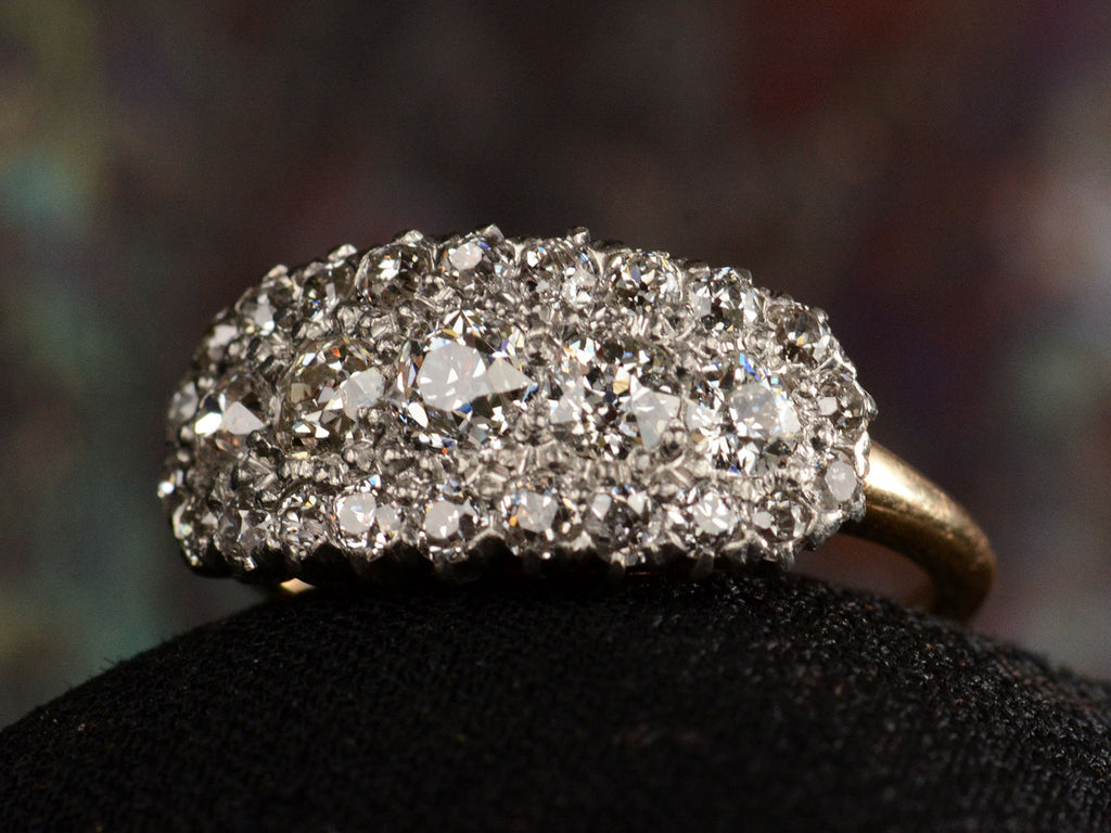 Right angled view of antique c1900 ring with an oval cluster of round old European cut diamonds set in platinum-topped 14K yellow gold, shown on dark background.