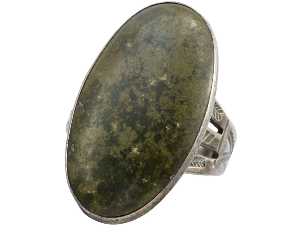 Angled view of a vintage Navajo ring with a large dark olive green cabochon bezel set in silver with a decorative stamped shank. Shown on white background.