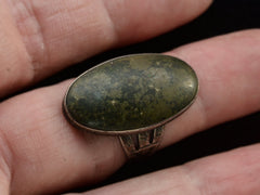 thumbnail of Angled view of a vintage Navajo ring with a large dark olive green cabochon bezel set in silver with a decorative stamped shank. Shown on finger.