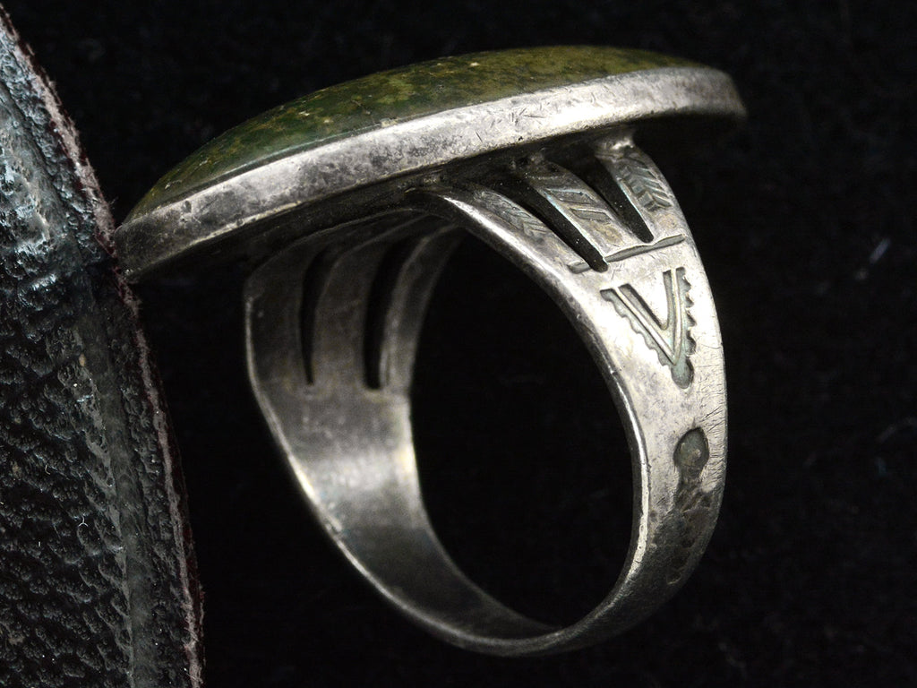 Detail view of shank of a vintage Navajo ring with a large dark olive green cabochon bezel set in silver with a decorative stamped shank. Shown on black background.