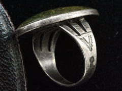 thumbnail of Detail view of shank of a vintage Navajo ring with a large dark olive green cabochon bezel set in silver with a decorative stamped shank. Shown on black background.