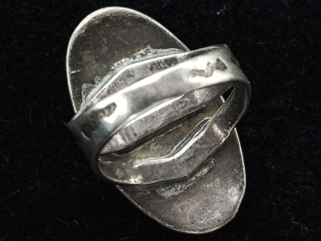 Reverse inside view of a Navajo ring with a large dark olive green cabochon bezel set in silver with a decorative stamped split shank. Shown on black background.