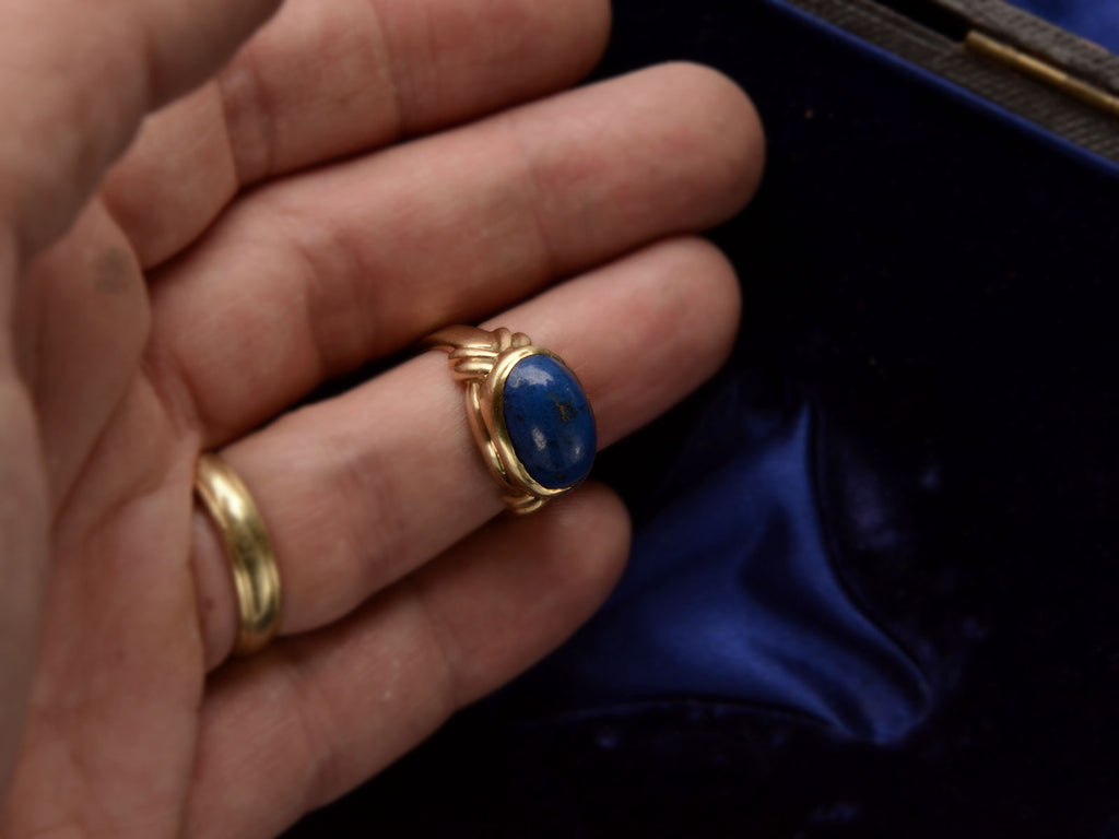 A vintage c1980 ring with an oval blue lapis lazuli set in 18K yellow gold, shown on finger.