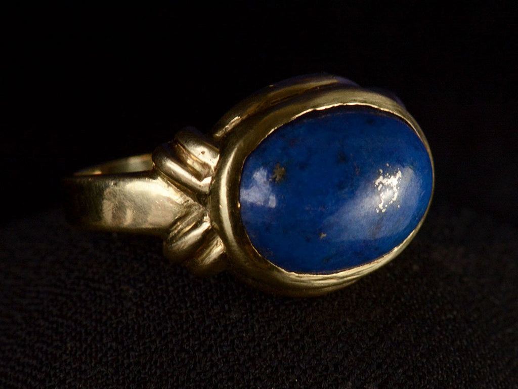 Opposite angled view of vintage c1980 ring with an oval blue lapis lazuli set in 18K yellow gold, shown on dark background.
