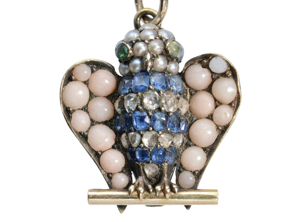 A owl pendant set with pale pink coral, sapphires, diamonds, pearls, and emeralds (shown on white background)