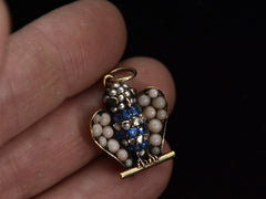 thumbnail of Antique c1890 owl pendant with pale coral wings, a pearl head, emerald eyes and a body of sapphires and rose cut diamonds. Shown on hand.