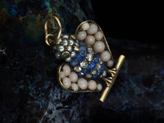 thumbnail of Angled top view of antique c1890 owl pendant with pale coral wings, a pearl head, emerald eyes and a body of sapphires and rose cut diamonds. Shown on dark background.