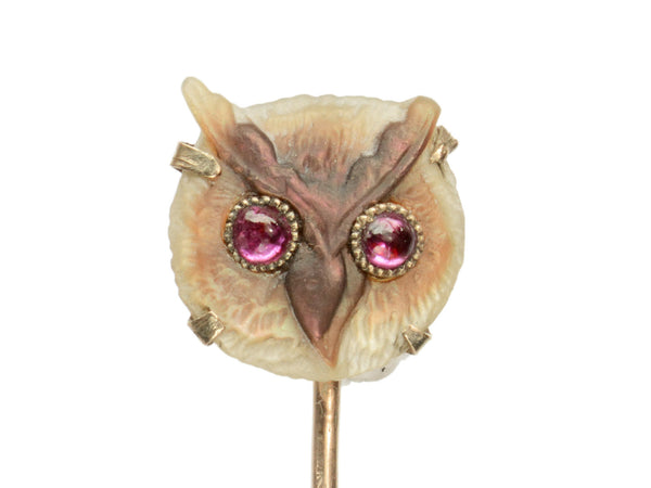 Detail of antique owl stick pin, carved from iridescent abalone and set with pink garnet eyes, shown on white background.