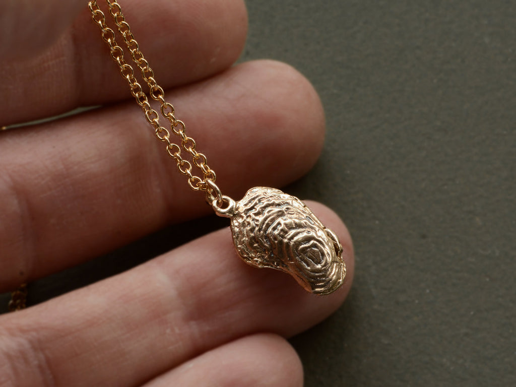 Oyster shaped gold pendant locket, shown held in hand.