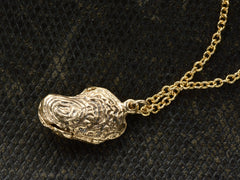thumbnail of Angled side view of oyster shaped gold pendant locket, shown on dark textured background.