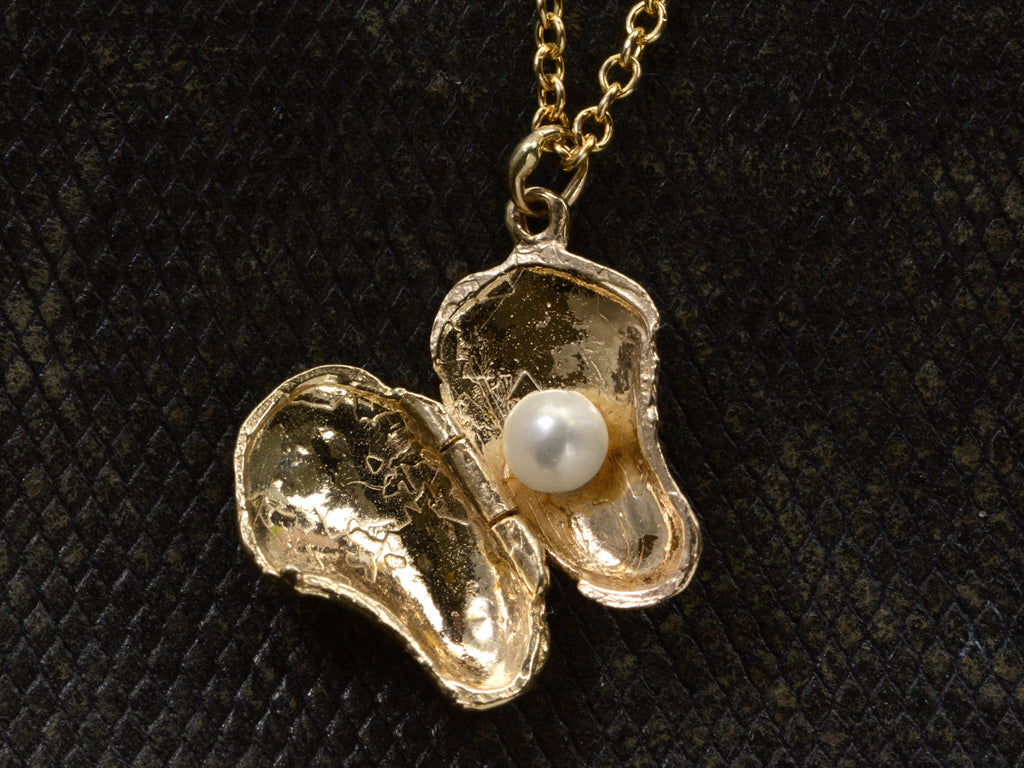Oyster shaped gold pendant locket, shown open with pearl inside, on dark textured background.