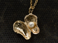 thumbnail of Oyster shaped gold pendant locket, shown open with pearl inside, on dark textured background.