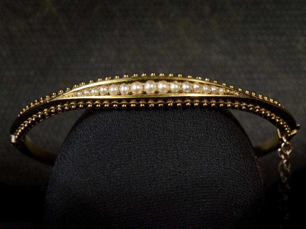 A narrow gold Victorian Pearl Bracelet with intricate Etruscan Revival granulation detailing, shown on dark background.