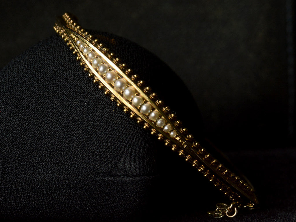 Front profile  of a narrow gold Victorian Pearl Bracelet with intricate Etruscan Revival granulation detailing shown on dark background.