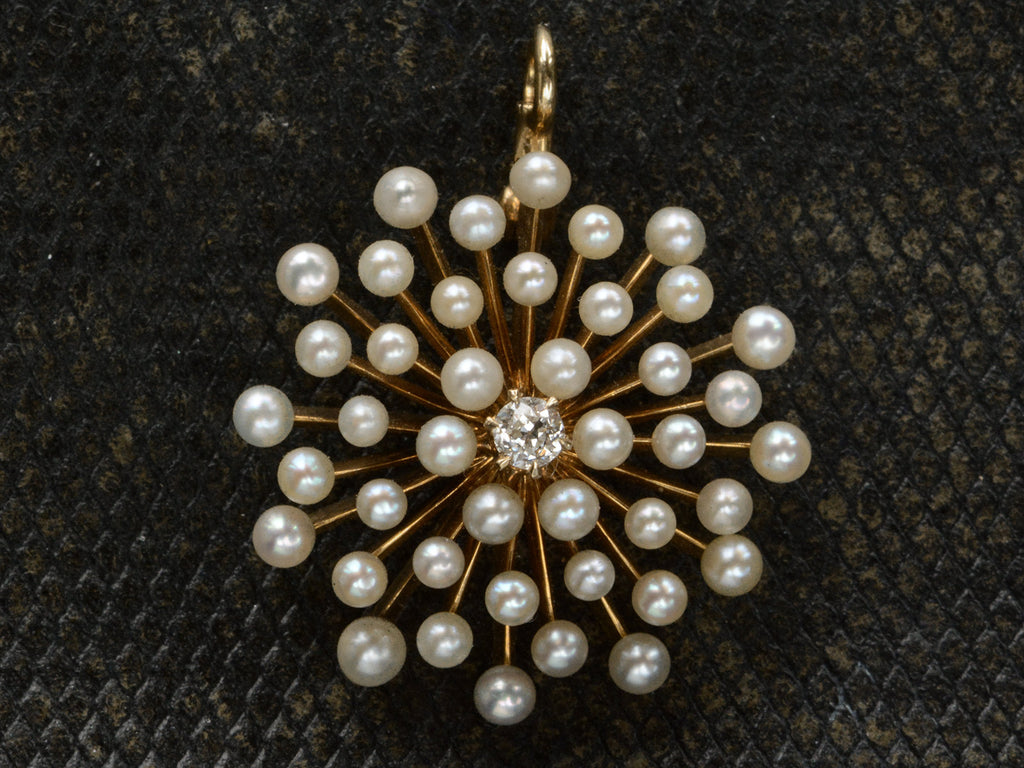 An antique starburst-form yellow gold pendant with pearls radiating out from a center diamond, shown on dark textured background.