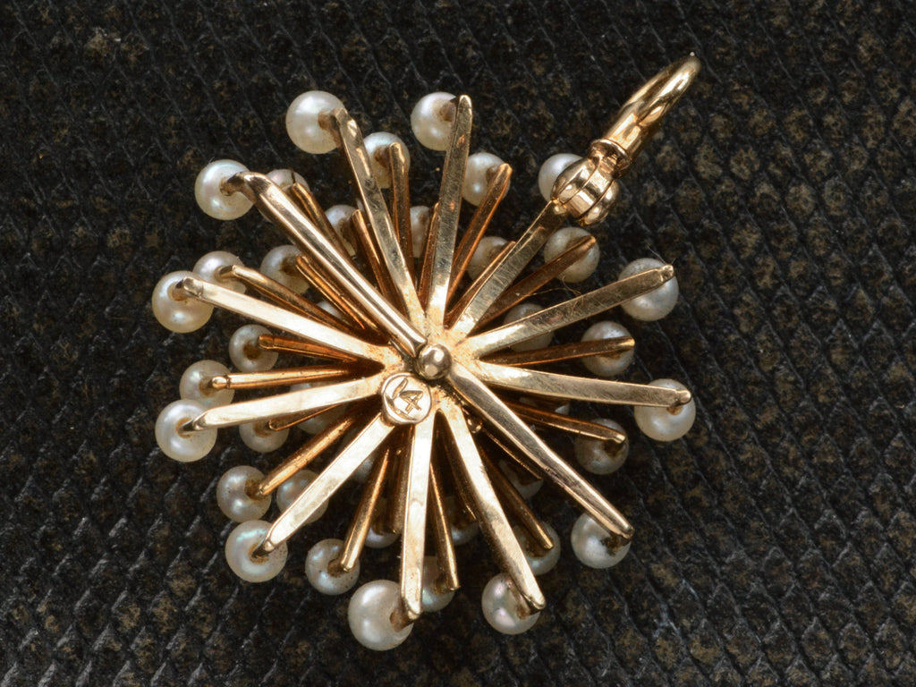 Reverse side of an antique starburst-form yellow gold pendant with pearls radiating out from a center diamond, shown on dark textured background. "14" stamp visible.