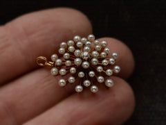 thumbnail of Angled view of an antique starburst-form yellow gold pendant with pearls radiating out from a center diamond, shown on hand.