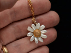 thumbnail of An antique daisy pendant with textured gold and pearl petals, shown on hand.