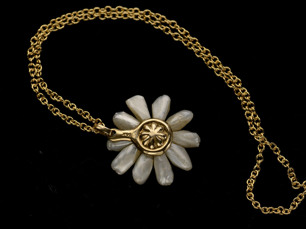 Reverse side of an antique daisy pendant with textured gold and pearl petals, shown on dark background.